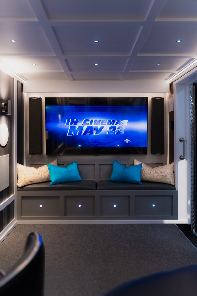 Home theatre inside the AVAS automation trailer with a large screen, in-wall speakers, and built-in seating