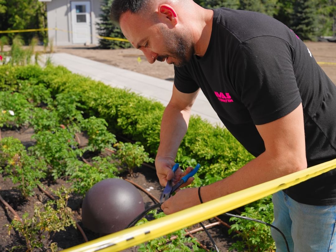 An AVAS technician wiring a landscape speaker in a garden bed