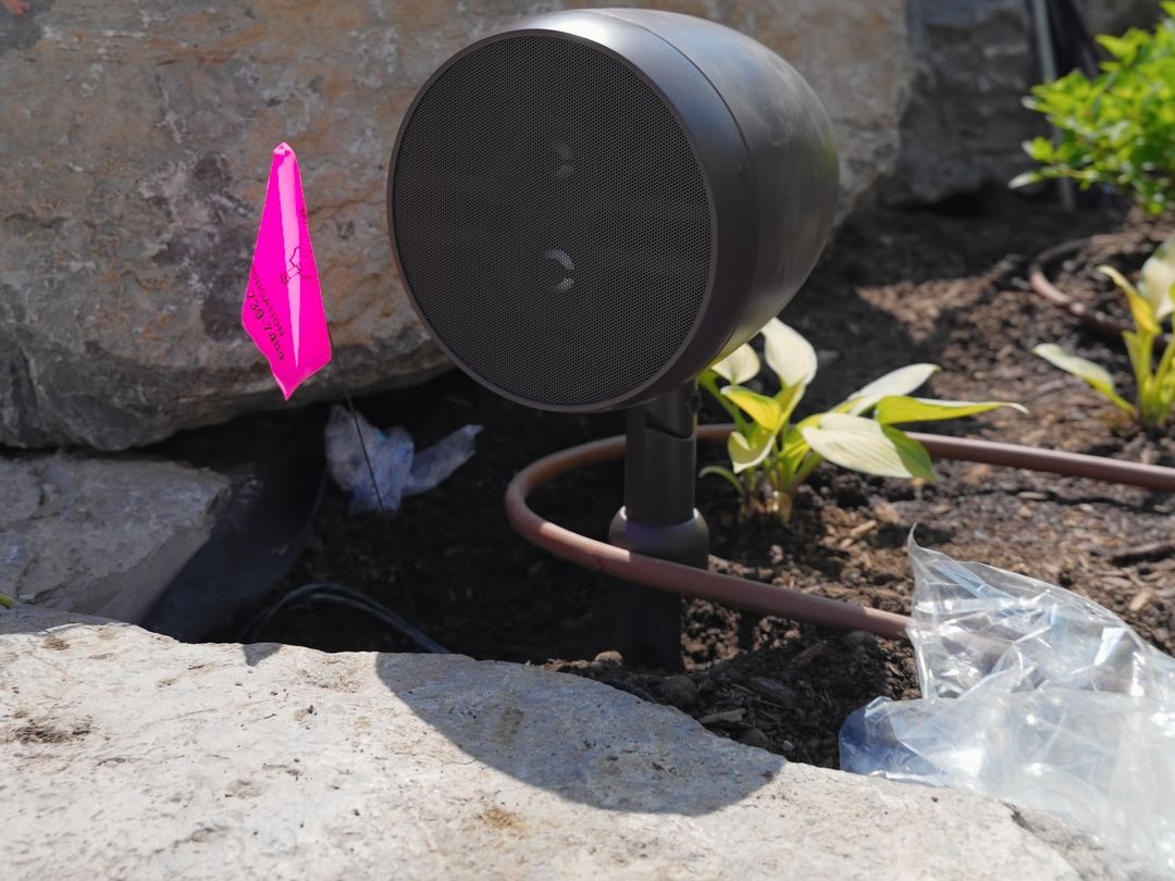 A landscape speaker installed beside a stone wall among the plants