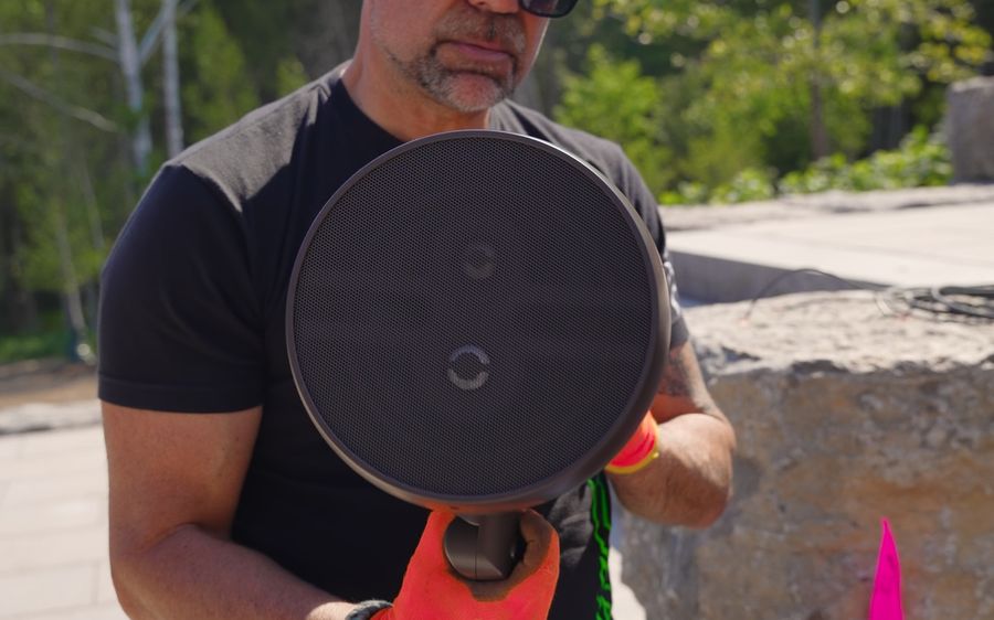 An AVAS technician holding an outdoor landscape speaker before installing it