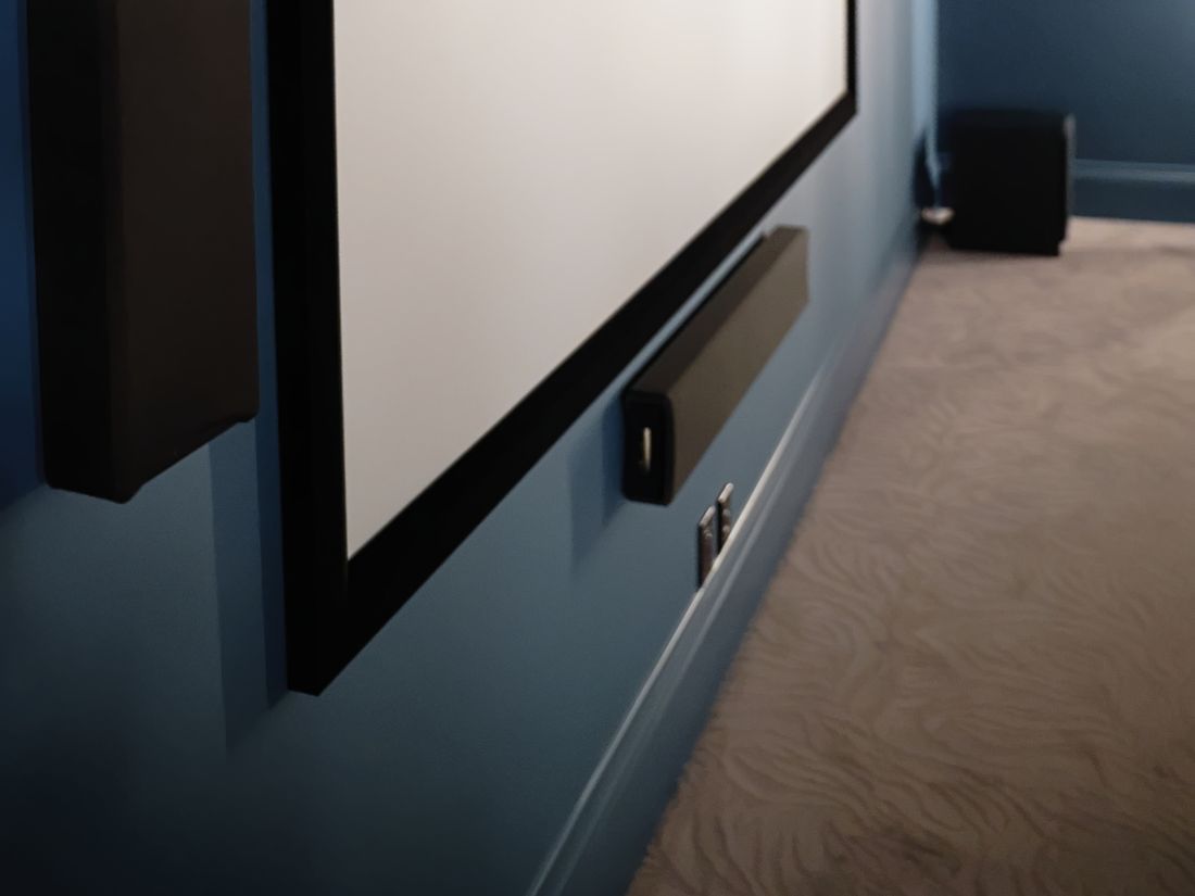 Front speakers and centre channel mounted around the screen, with a subwoofer in the corner