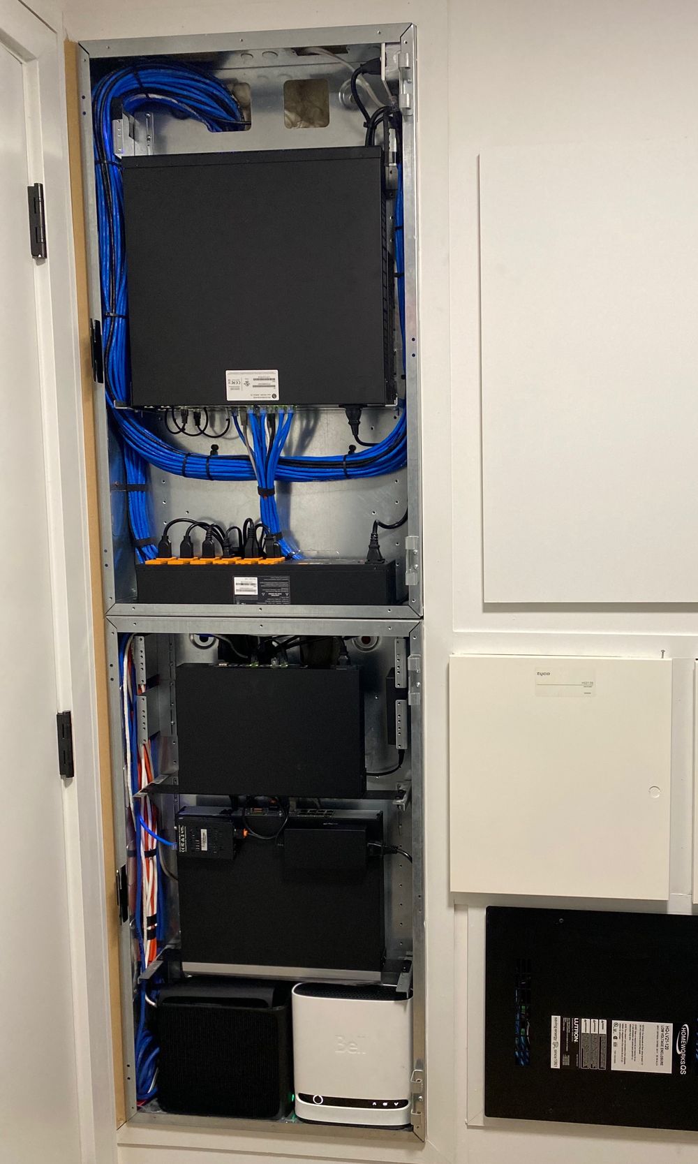 The same in-wall equipment rack after the AVAS takeover, with every device mounted and the network cables dressed and bundled