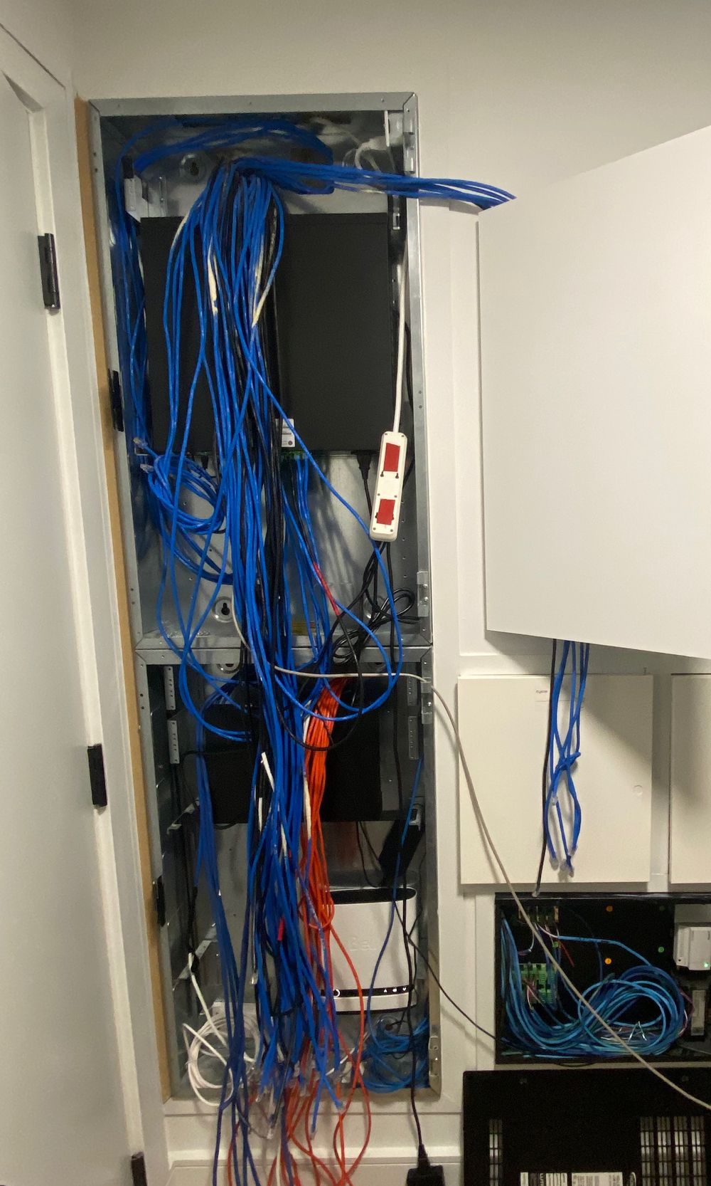 An in-wall equipment rack before the AVAS takeover, with tangled network cables hanging out of the wall and spilling onto the floor