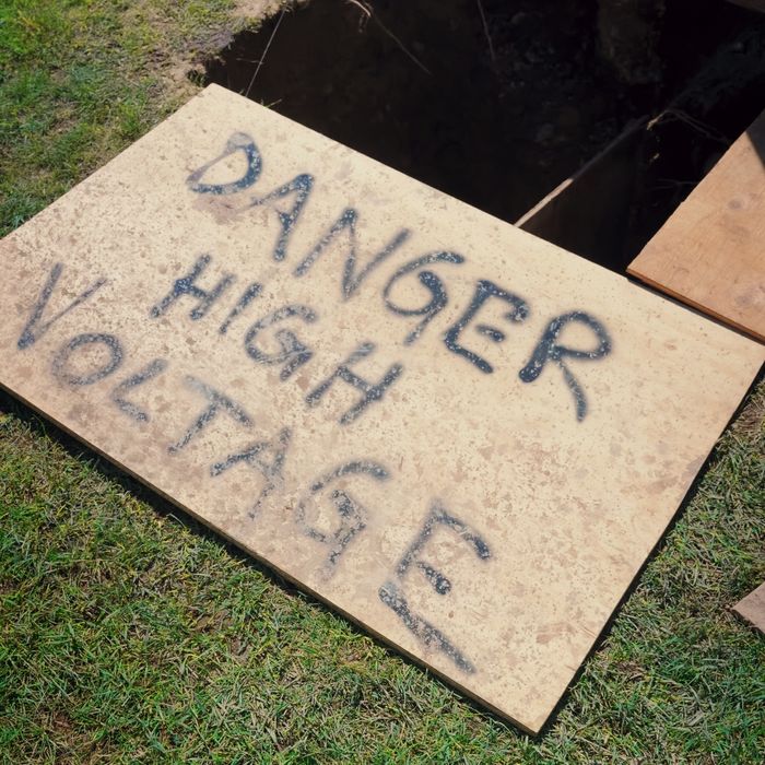 A hand painted danger high voltage sign on plywood covering the dig site