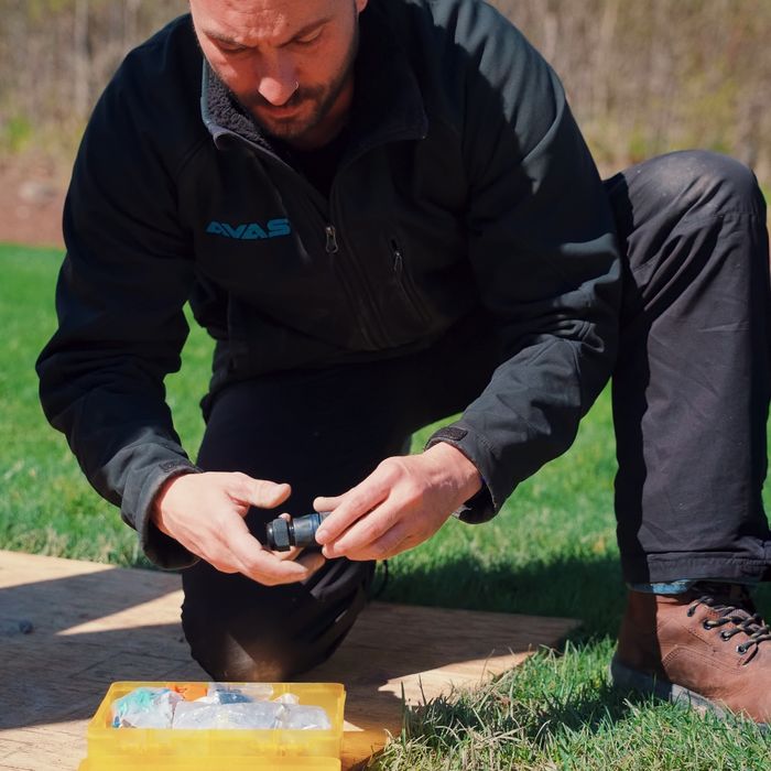 An AVAS technician kneeling on the lawn preparing wire connectors beside the dig