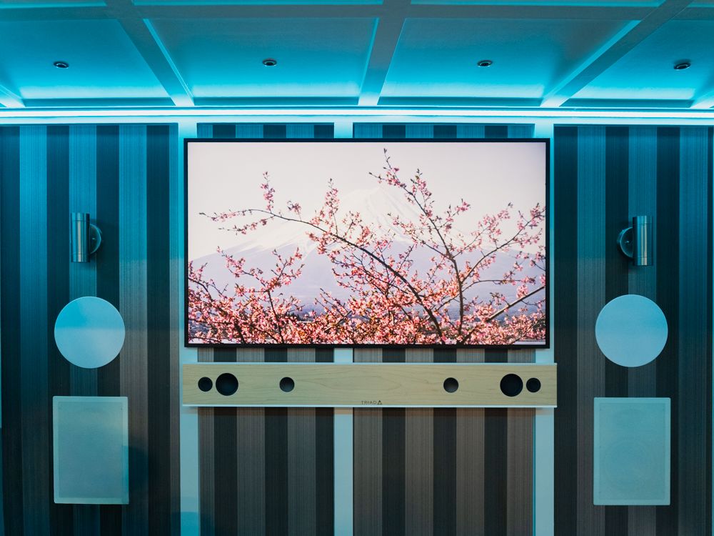 The trailer lounge wall lit in cool blue, a TV showing cherry blossoms between two speakers