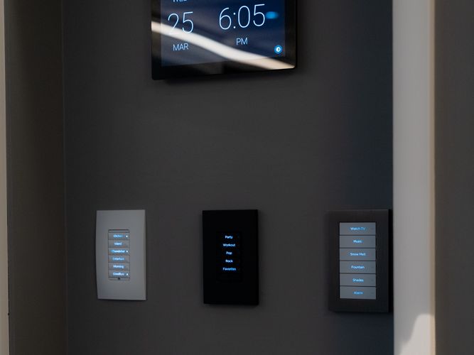 Control4 touchscreen and three keypads on a dark wall