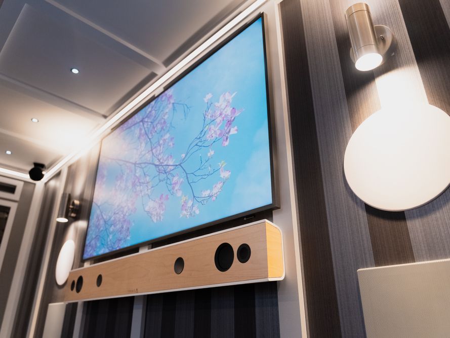Wood soundbar under a TV beside a wall sconce inside the trailer