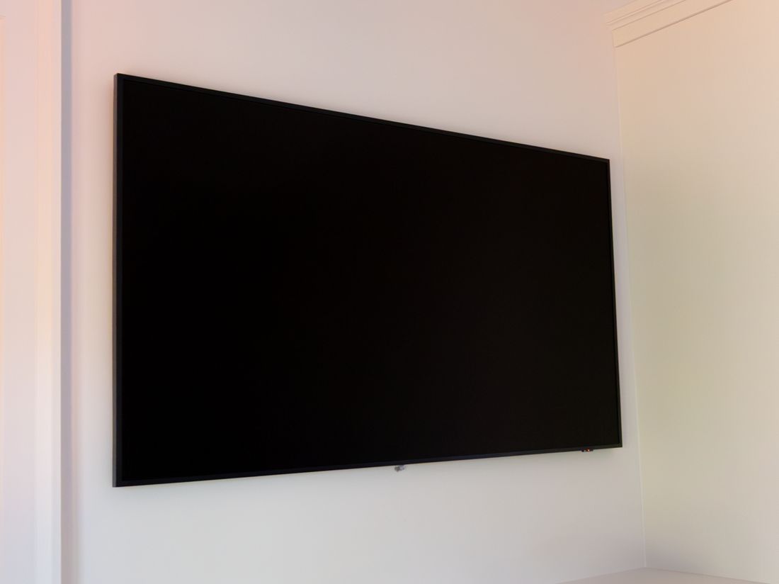 A large bedroom TV mounted above a white dresser with no boxes or cables in sight