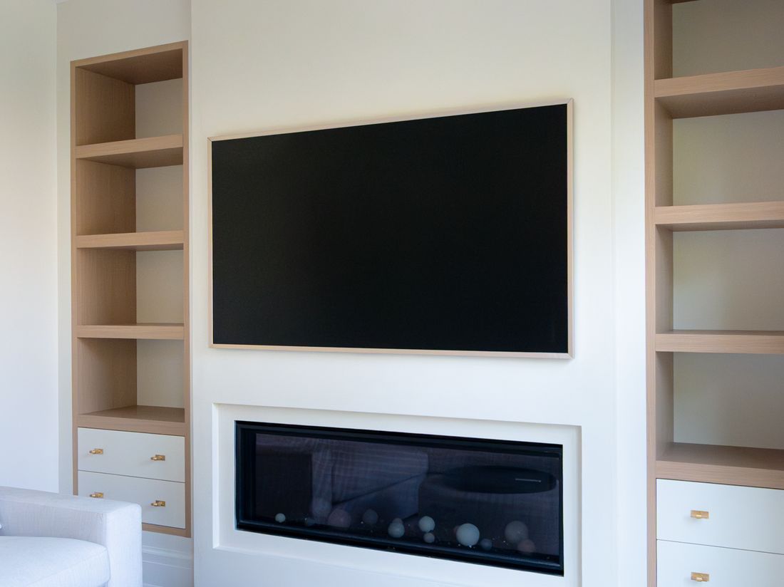 A TV set flush into white oak built-ins above a linear fireplace