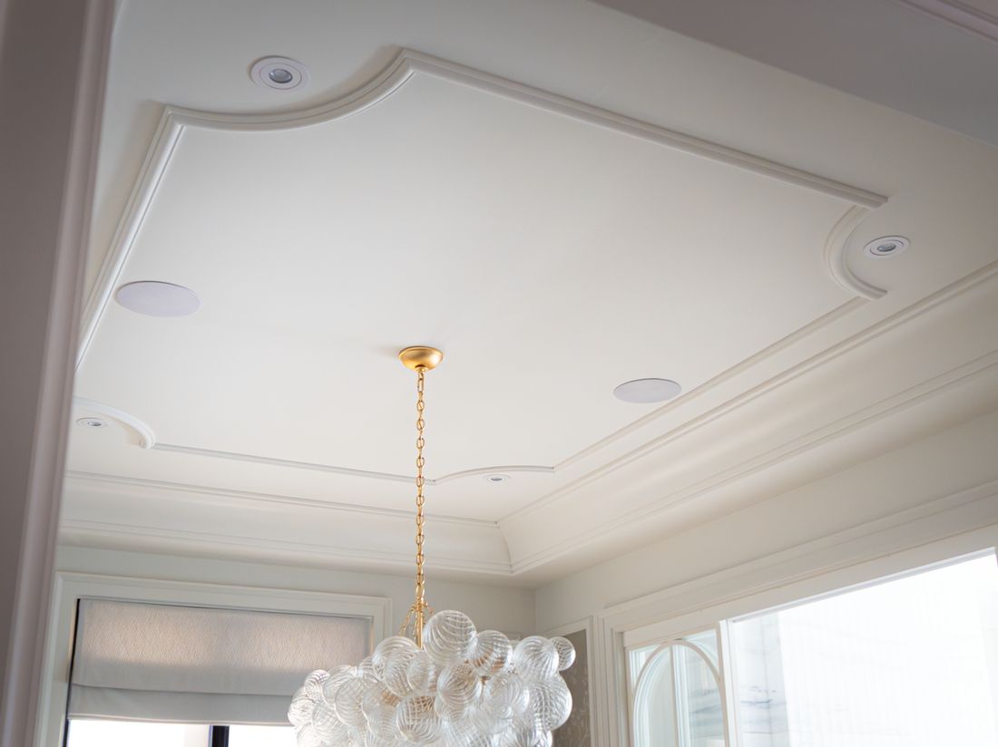 A dining room tray ceiling with a glass chandelier and discreet ceiling fixtures