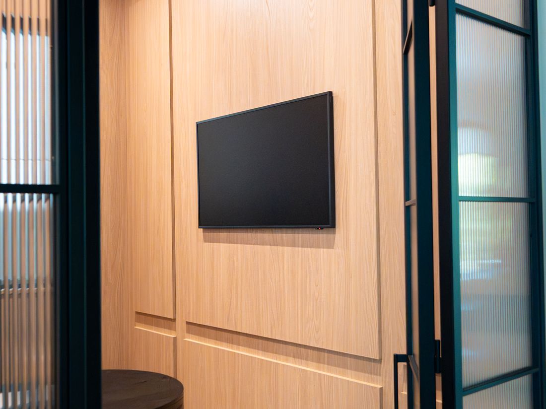 A wood panelled home office with a wall mounted TV behind glass doors