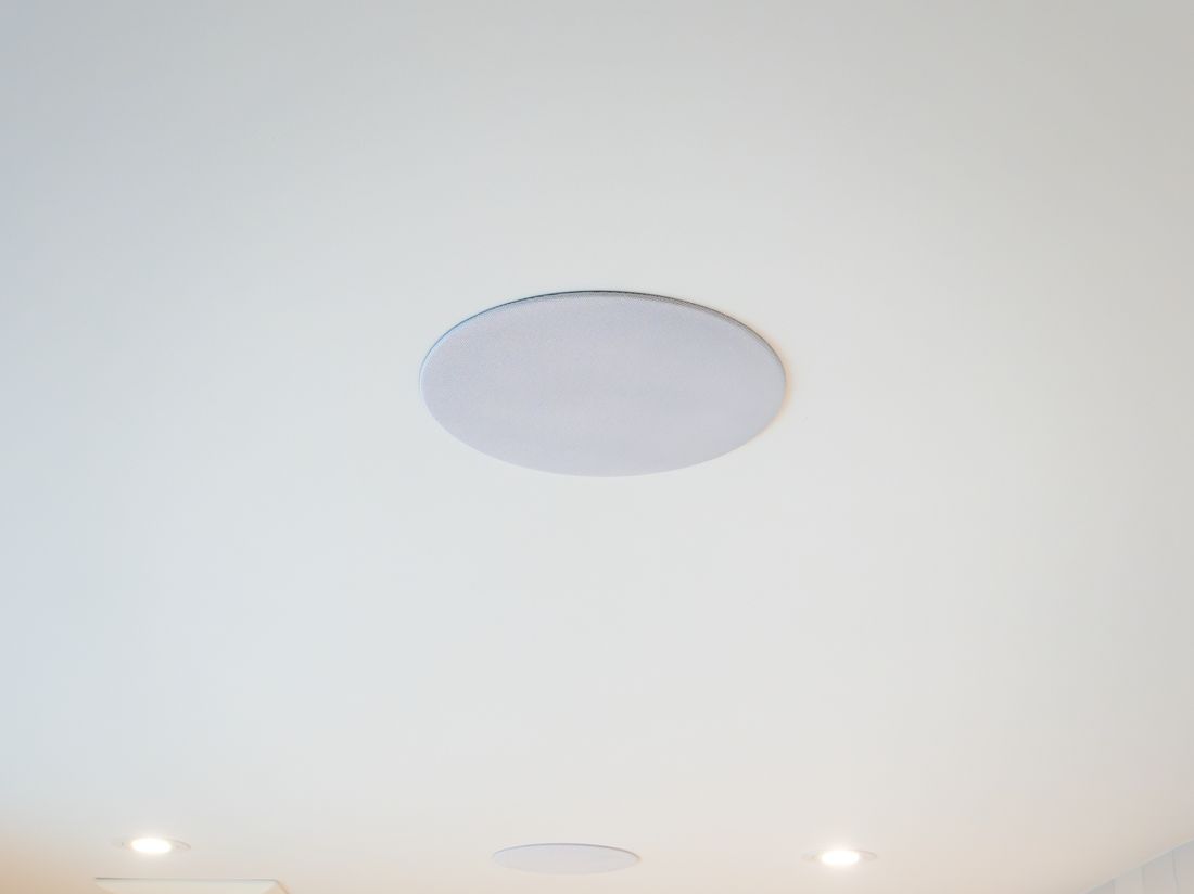 A flush white in-ceiling speaker above a pair of arched vanity mirrors