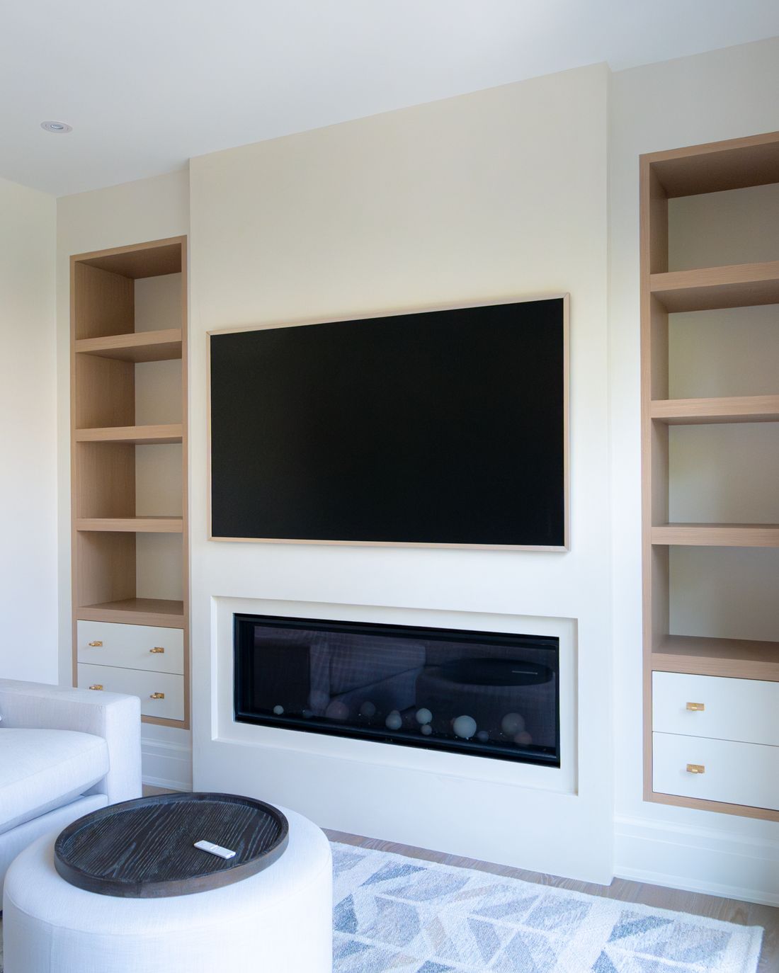 A bright family room with a TV set into white built-ins above a linear fireplace, part of a whole home audio and video system