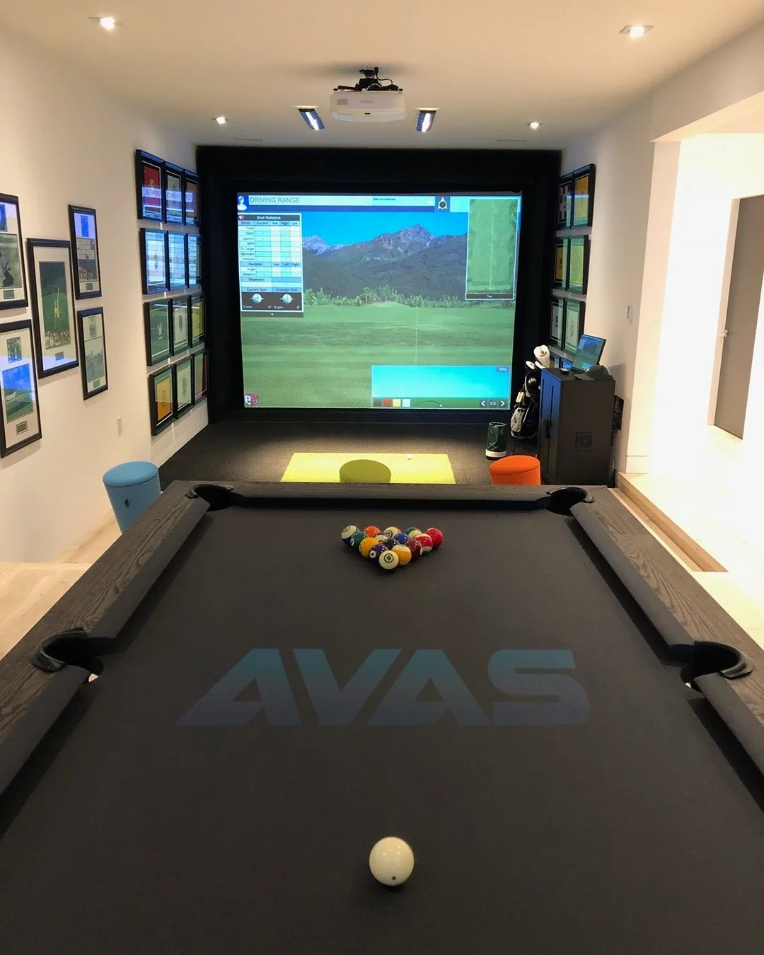 A golf simulator screen at the end of a games room, with a billiards table in front