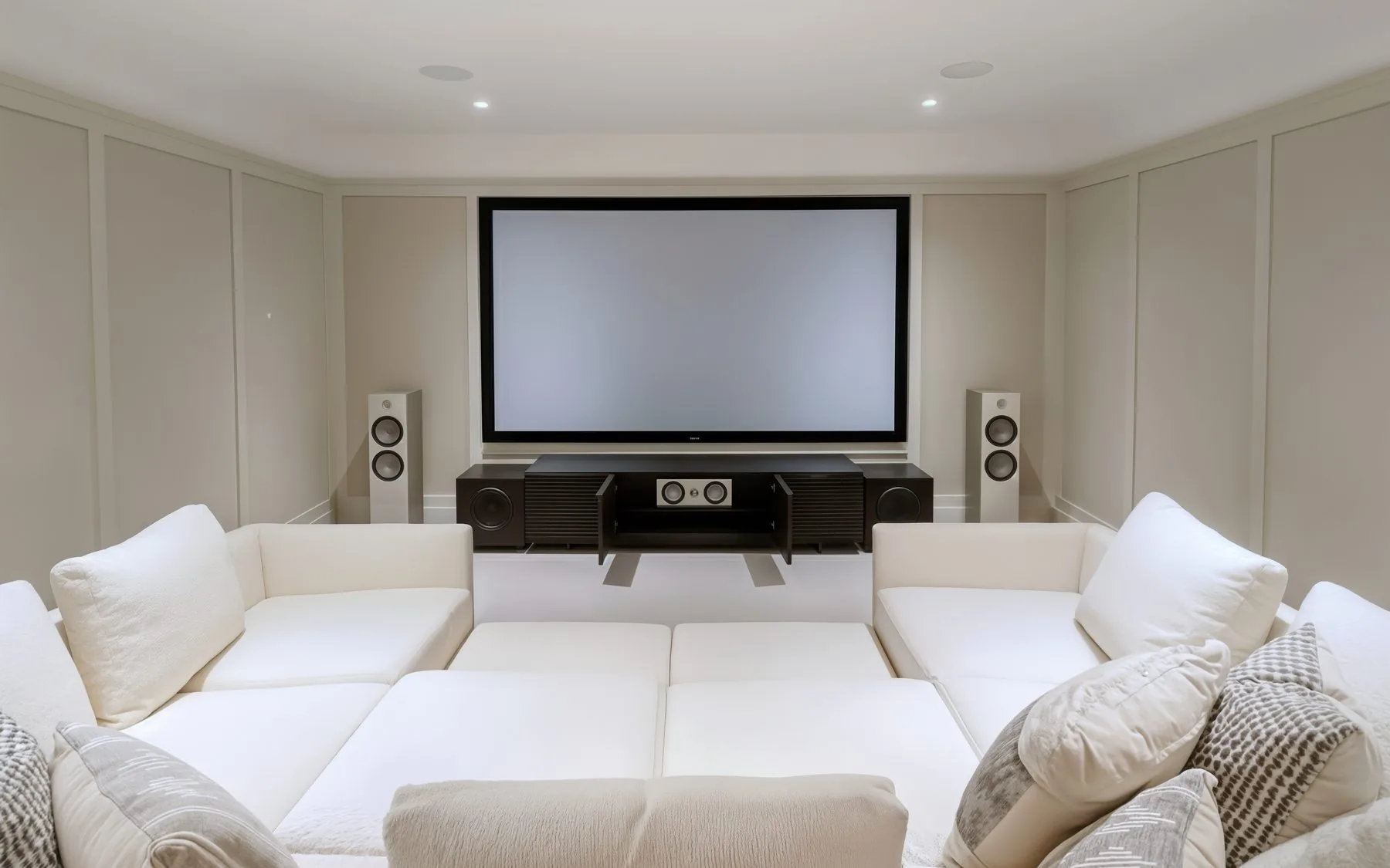 A dedicated home theatre in The Blue Mountains with a large screen, two tower speakers and a deep white sectional