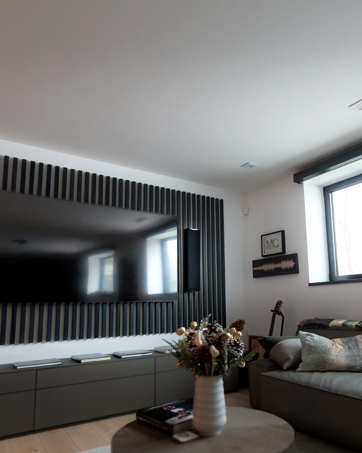 A family room with a dark wood slat wall around the TV and a motorized shade on the window