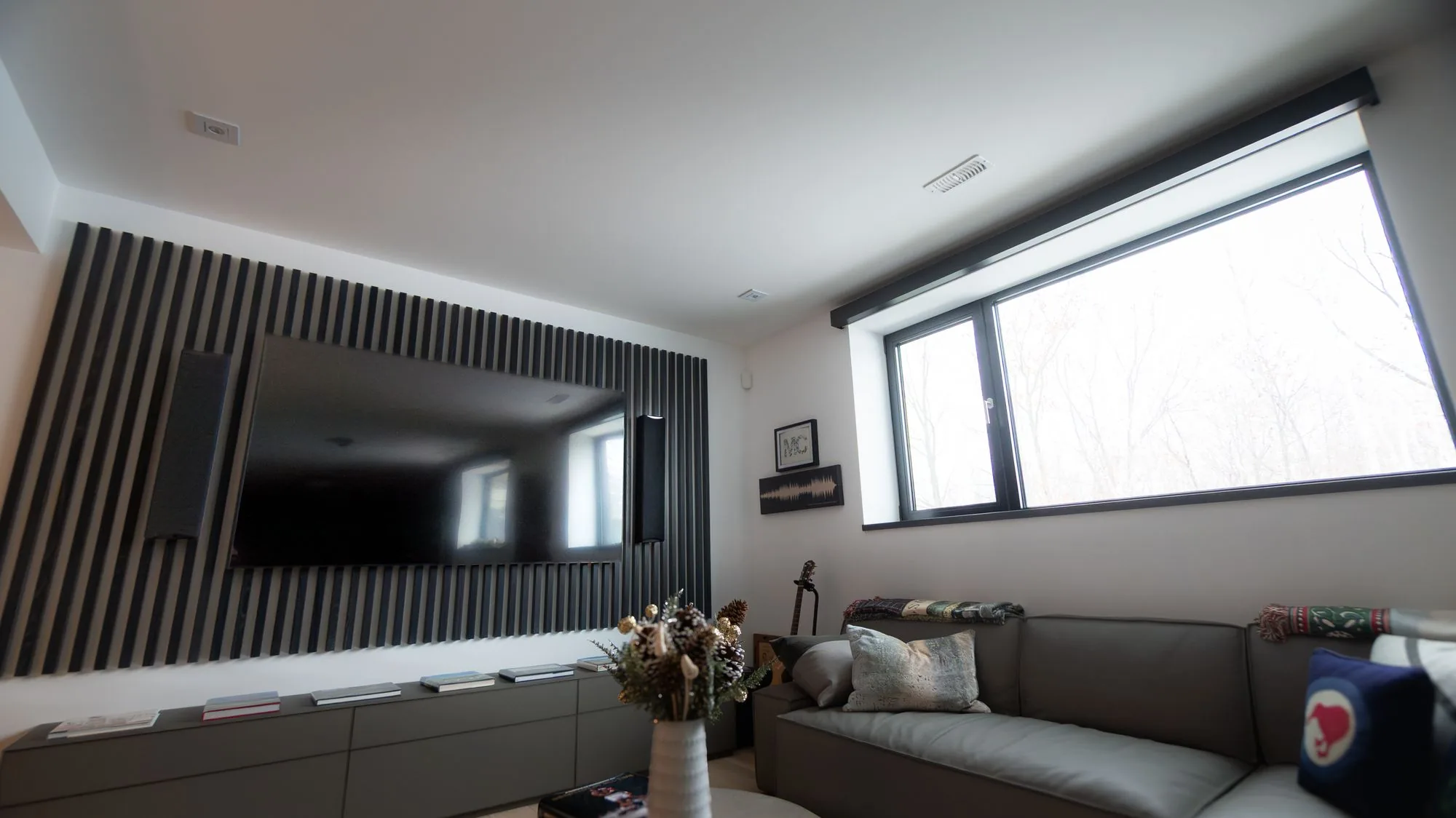 A media room with a dark wood slat wall, a TV and a window shade