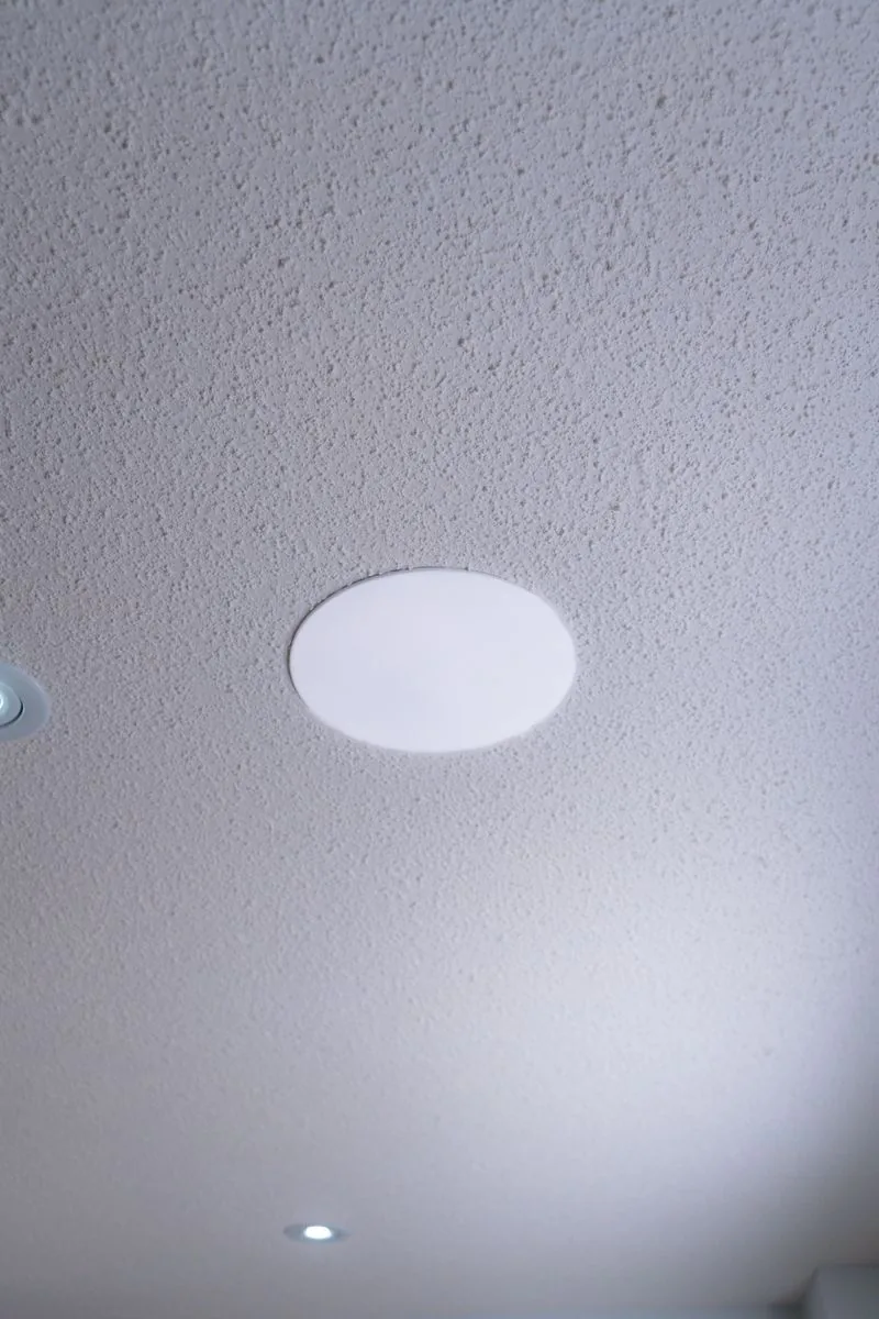 A round in-ceiling speaker on a white ceiling