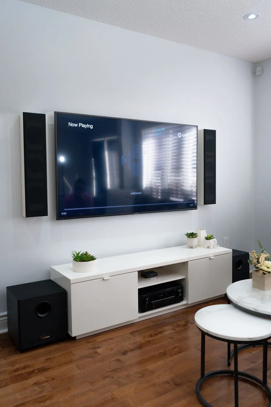 A living room theatre TV wall with a slim speaker on each side of the TV and a subwoofer at each end of the low console