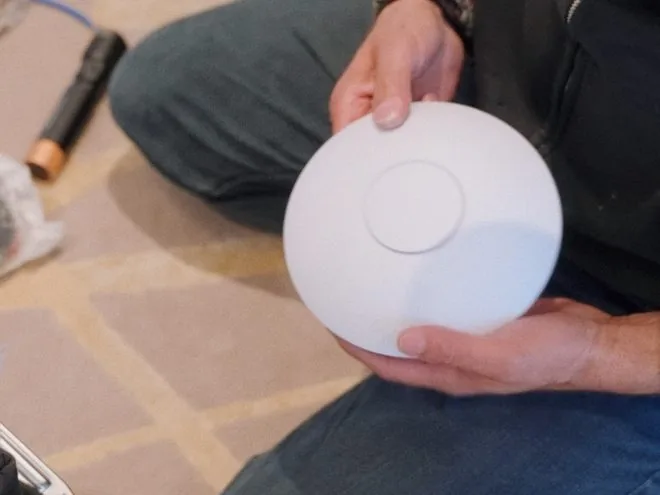 An AVAS technician holding a ceiling WiFi access point before mounting it
