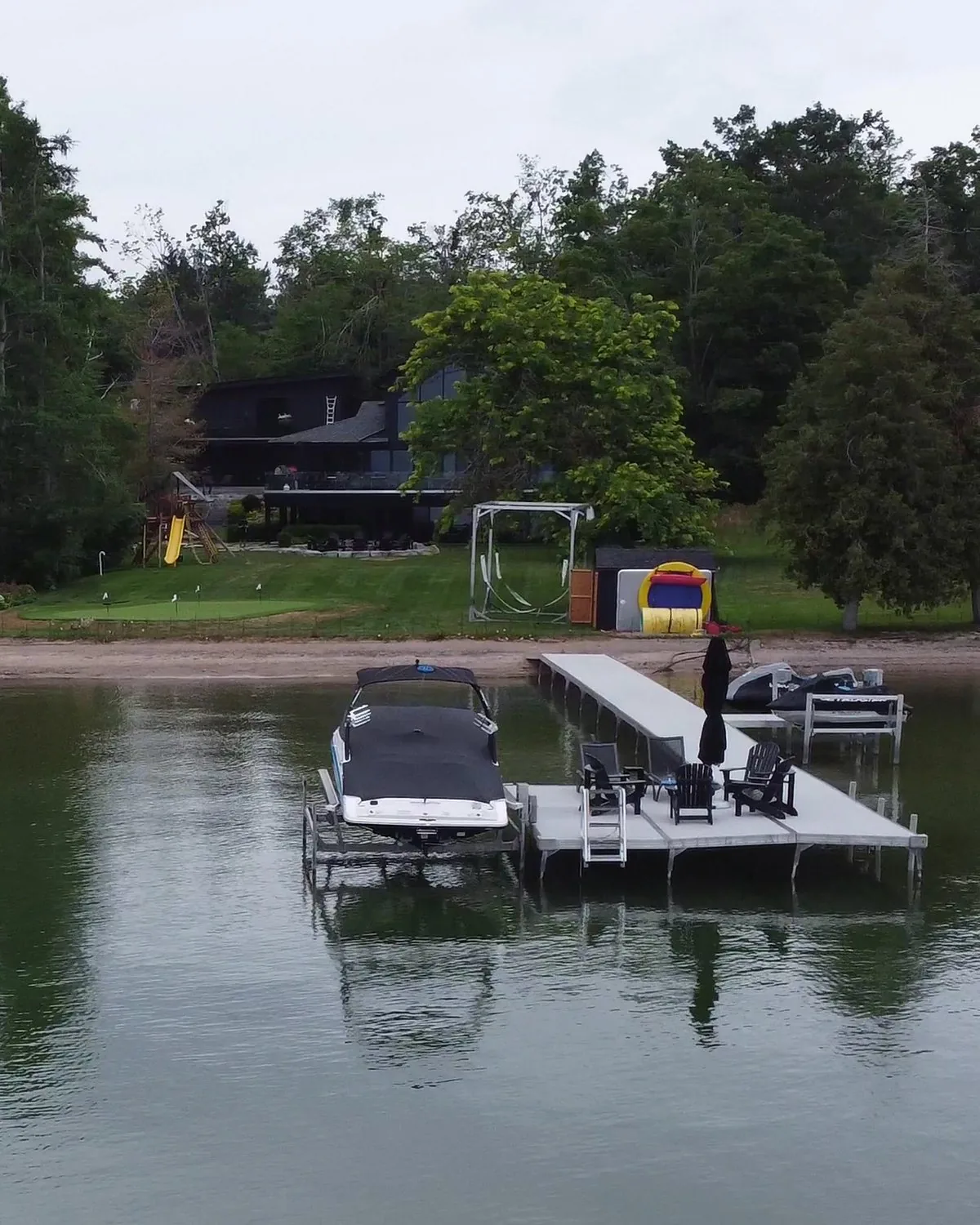 A lakeside cottage dock with a boat and chairs, seen from a drone