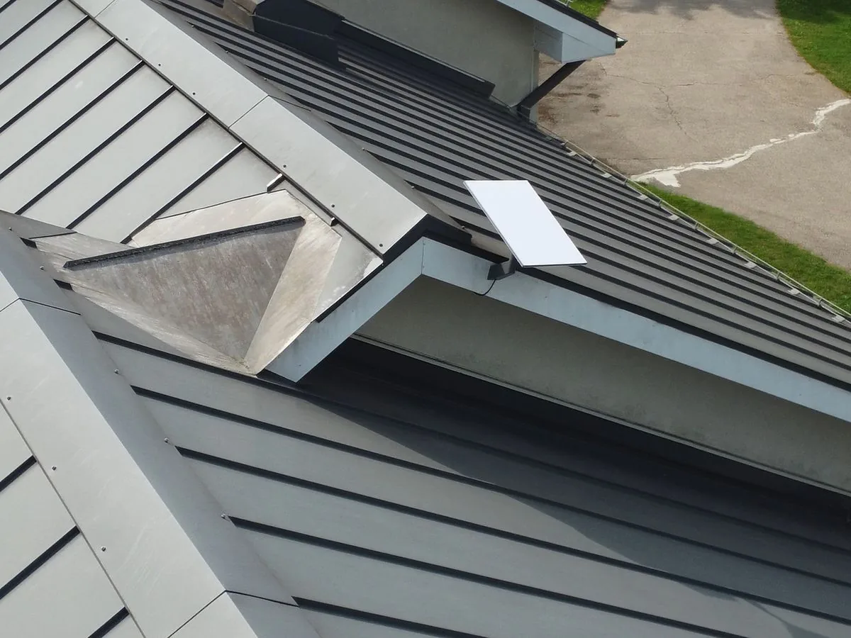 A white Starlink dish on a bracket at the edge of a standing seam metal roof