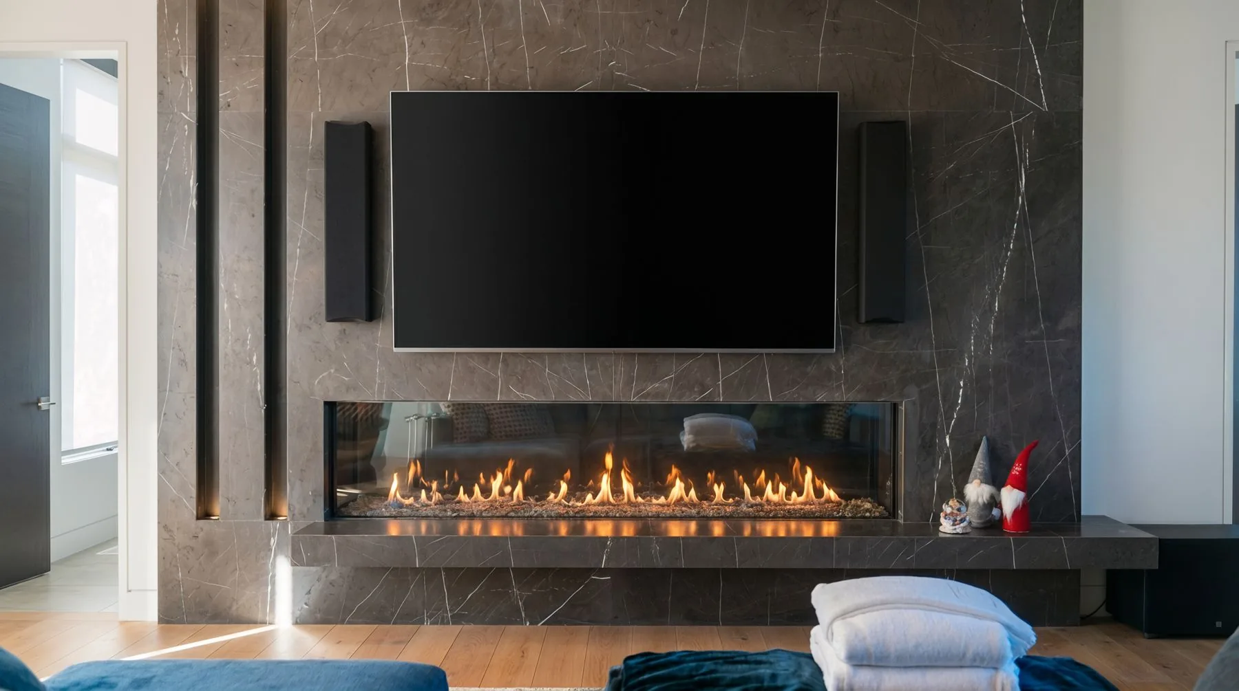 A living room wall with the TV and speakers set into stone above a linear fireplace