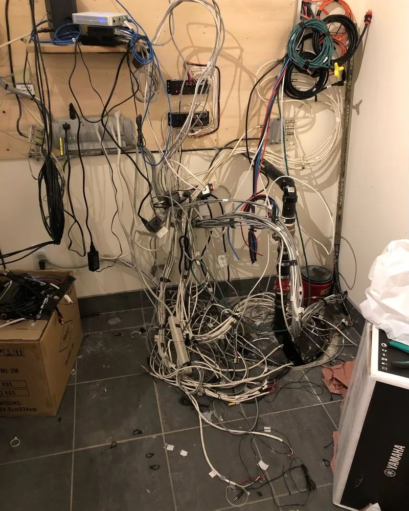 A wall of loose cables, power bars and boxes hanging in a basement corner